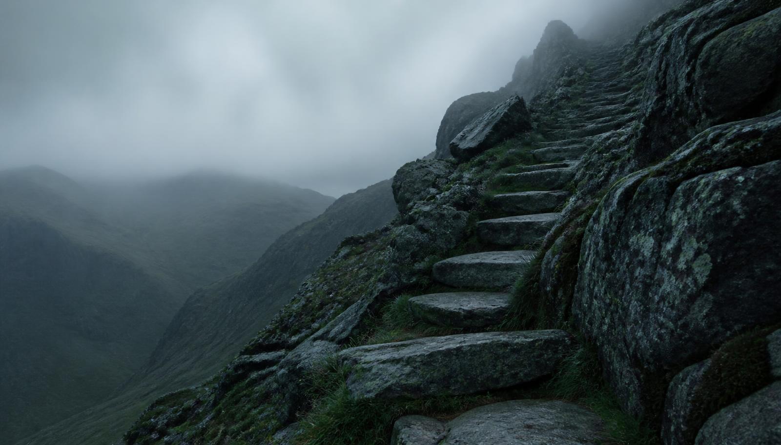 A stepped rocky ascent rising through mist, the obstacles on the route visible
